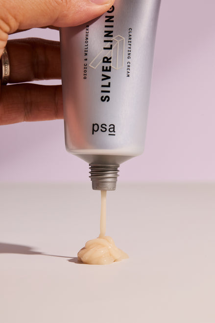 Hand holding a tube of 'Silver Lining' cream with visible cream being squeezed out on a light background